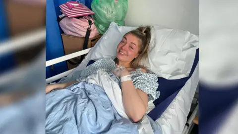 Mathilde Barker A woman lying in a hospital bed, she is smiling at the camera. 