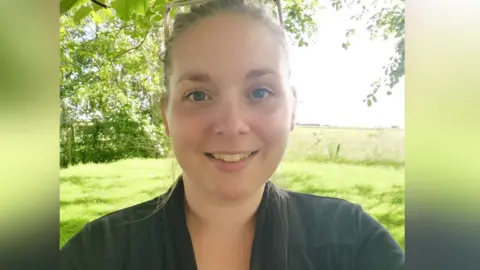 Emma Blackburn A selfie of a women standing in a field. She is wearing a black top and is smiling at the camera. 