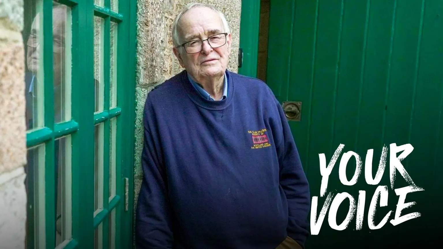BBC An older man with grey receding hair and glasses leans against a granite wall looking towards the camera. He wears khaki, flannel trousers and a blue sweatshirt. He looks sad.