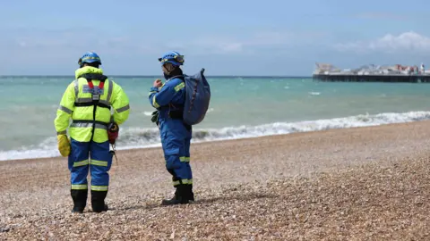 Charlotte Coney / Getty Images Two responders in reflective gear stand on the pebble beach of Brighton looking out to sea with the Brighton pier in the background on Wednesday.